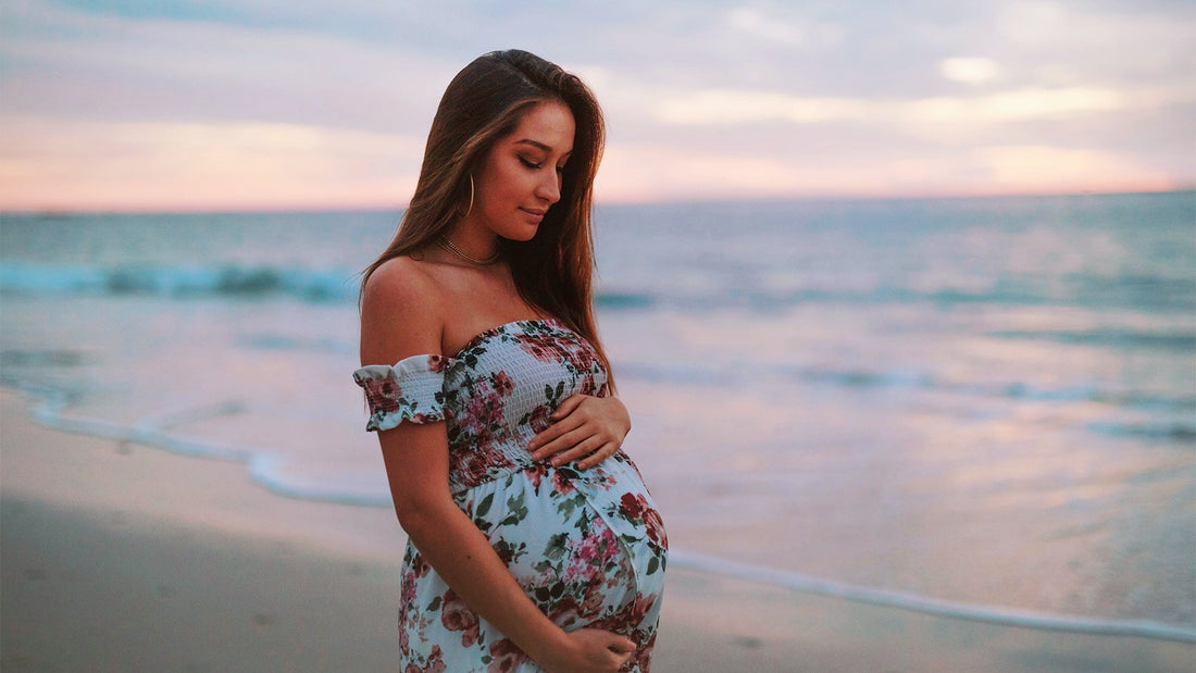 Femme devant une plage tenant son ventre de femme enceinte